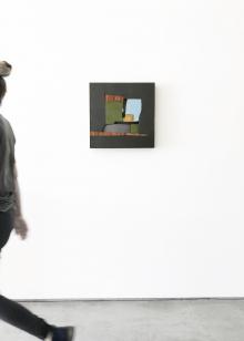 A person walking by a mixed media piece in black, brown, green, and blue by artist Pascal Pierme 